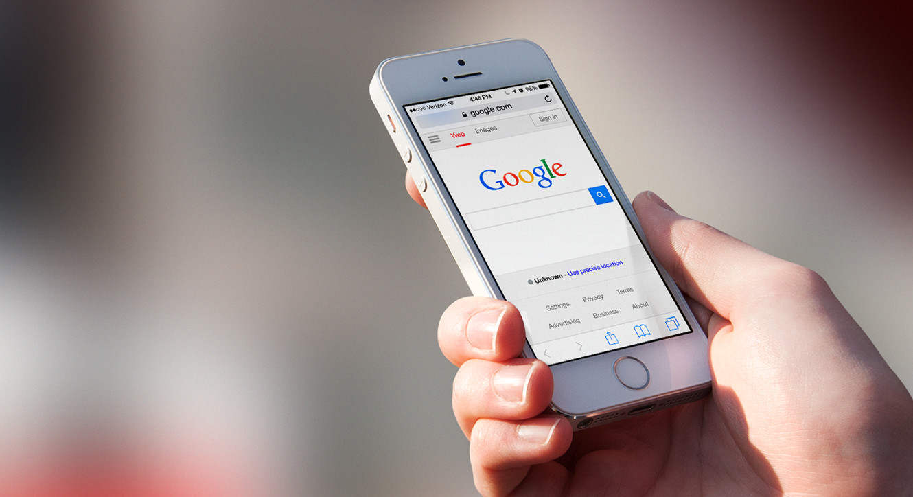A person holds an iPhone displaying the Google search homepage on a mobile device.